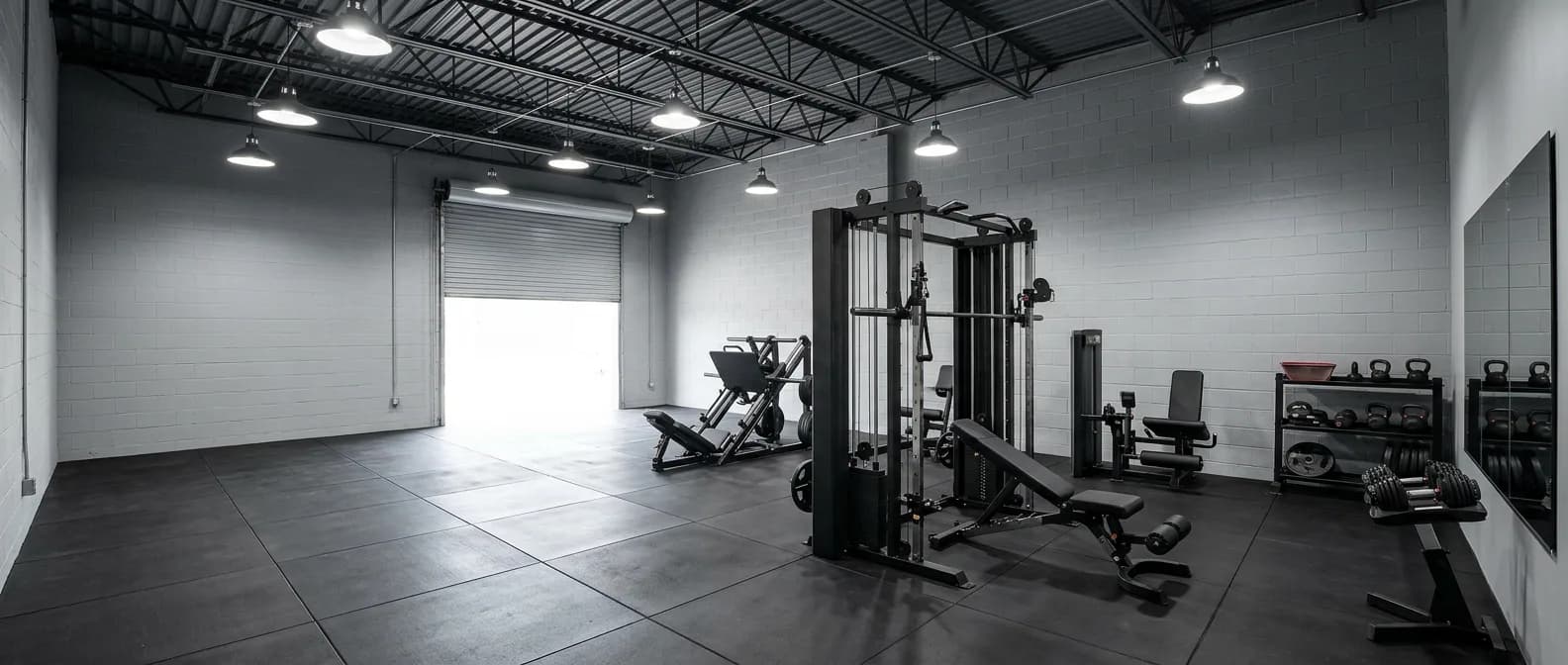 Fully equipped bodybuilding gym in a small warehouse: functional trainer, leg press, benches, dumbbells and kettlebells on rubber flooring